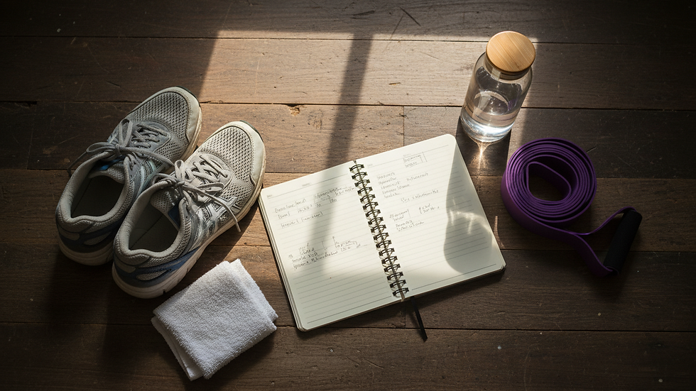 Overhead view of a fitness journal beside water, resistance bands, and running shoes.