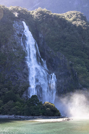 Mächtiger Wasserfall stürzt zwischen Regenwald und Felsen in den Milford Sound im Fiordland Nationalpark