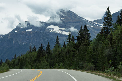 Geschwungene Straße des Icefields Parkway vor dramatischer Bergkulisse in den Rockies.