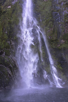 Nahaufnahme eines mächtigen Wasserfalls mit dichter Gischt an einer Felswand im Milford Sound.