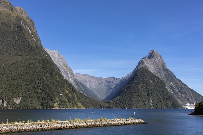 Spektakuläre Bergkulisse am Milford Sound mit blauem Wasser und Kreuzfahrtschiff im Fiordland Nationalpark