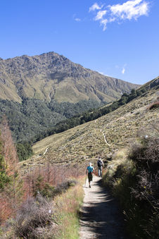 Wanderer auf dem Ben Lomond Track oberhalb von Queenstown zwischen Tussockgras und beeindruckender Berglandschaft