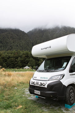 Unser Camper auf dem Cascade Creek Campsite vor den wolkenverhangenen Bergen des Fiordland National Parks.