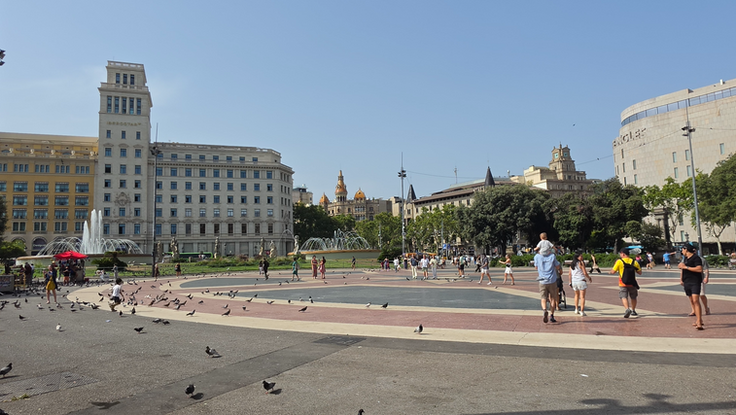 Panorama der Plaça de Catalunya mit Brunnen, Tauben und Spaziergängern in Barcelona.