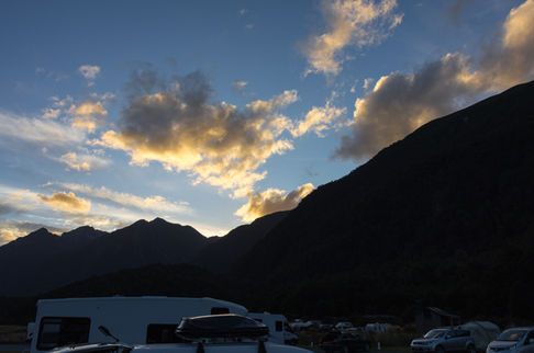 Abendstimmung über dem Campingplatz mit dunklen Bergsilhouetten und leuchtenden Wolken im Fiordland.