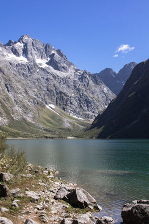 Blick über den Lake Marian auf schroffe Berggipfel und Schneefelder im Fiordland Nationalpark.