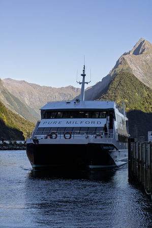 Ausflugsschiff Pure Milford am Anleger vor den steilen Bergen des Milford Sound im Fiordland Nationalpark.