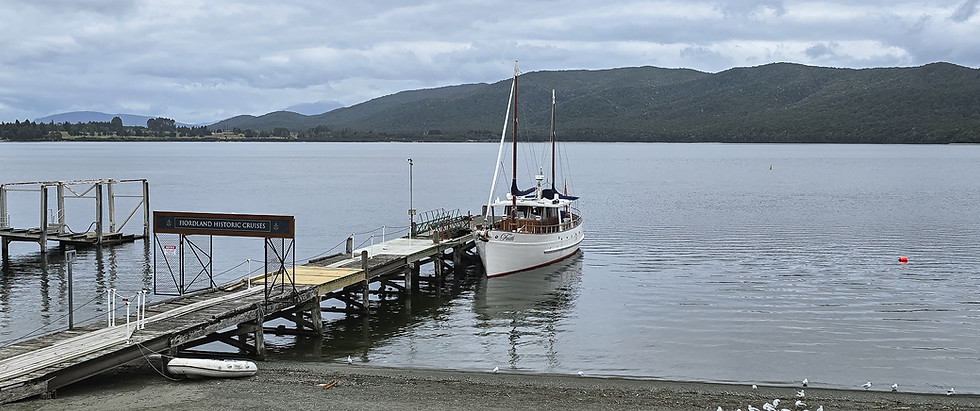 Historisches Ausflugsschiff am Steg des Lake Te Anau mit bewaldeten Bergen im Hintergrund in Neuseeland.