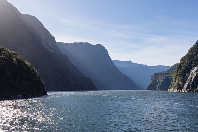 Weiter Blick über den Milford Sound zwischen hohen Felswänden bei sonnigem Wetter im Fiordland Nationalpark.