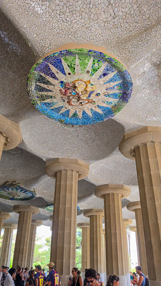 Mosaikdecke der Säulenhalle im Park Güell mit farbenfrohem Keramikmedaillon und Gaudís Architektur.