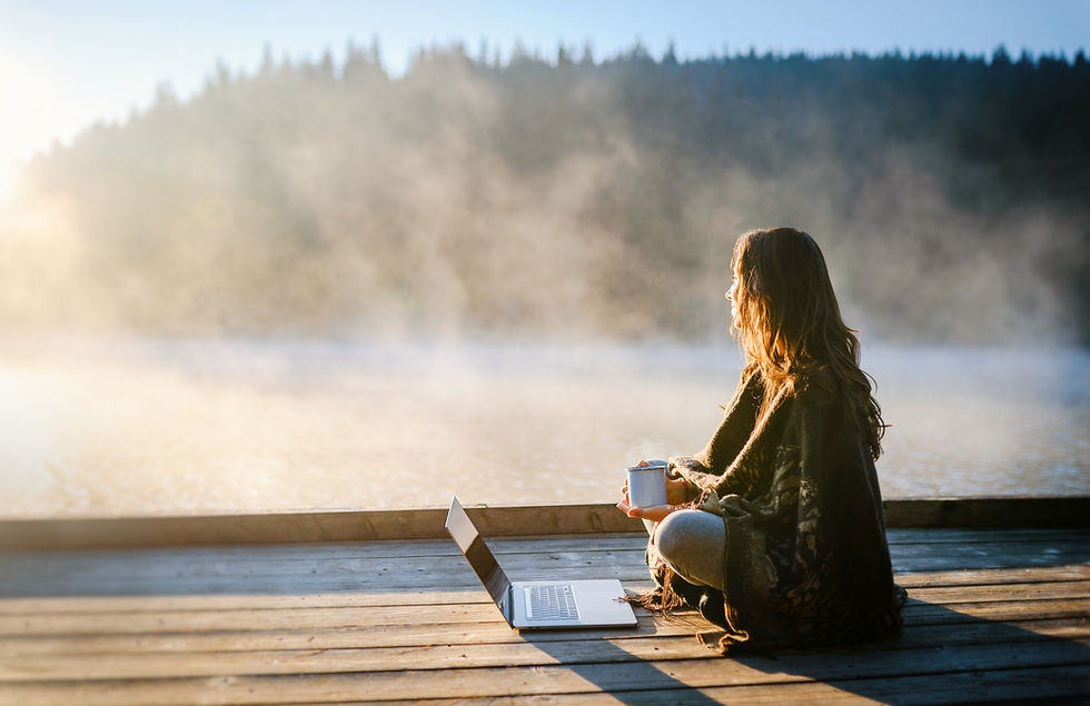 woman with computer on the dock of a peaceful lake surrounded by mist on a sunny day
