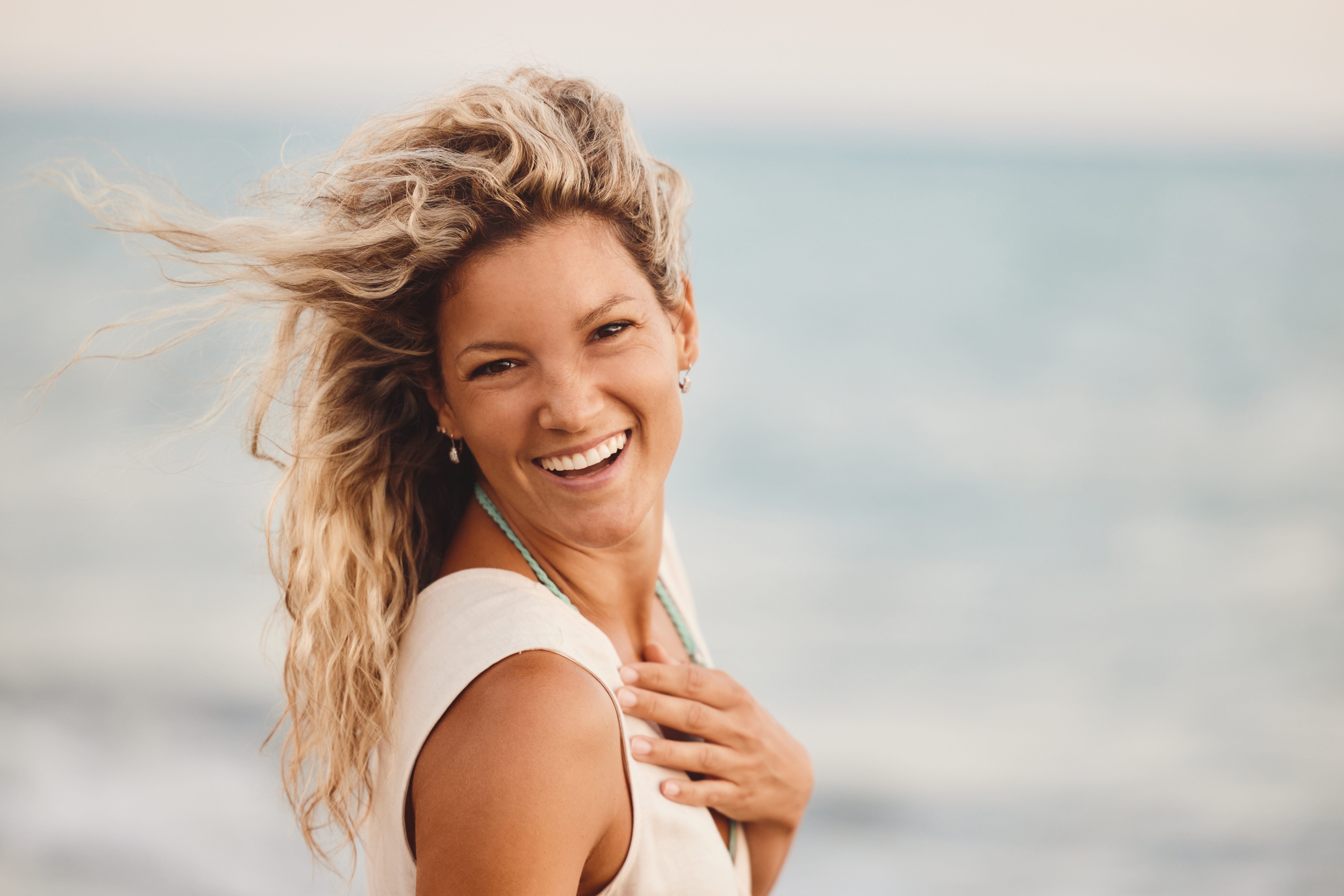 Smiling woman with windswept blonde hair by the ocean