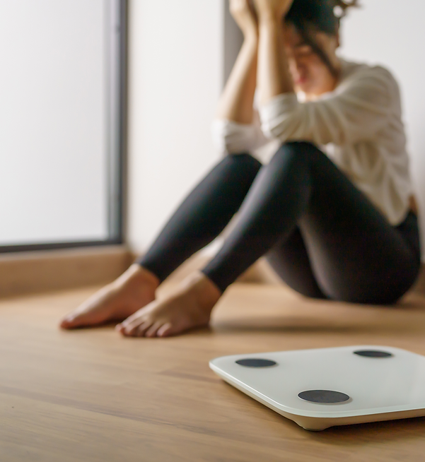 young woman crouched in corner with head in hands and a bathroom scale near her