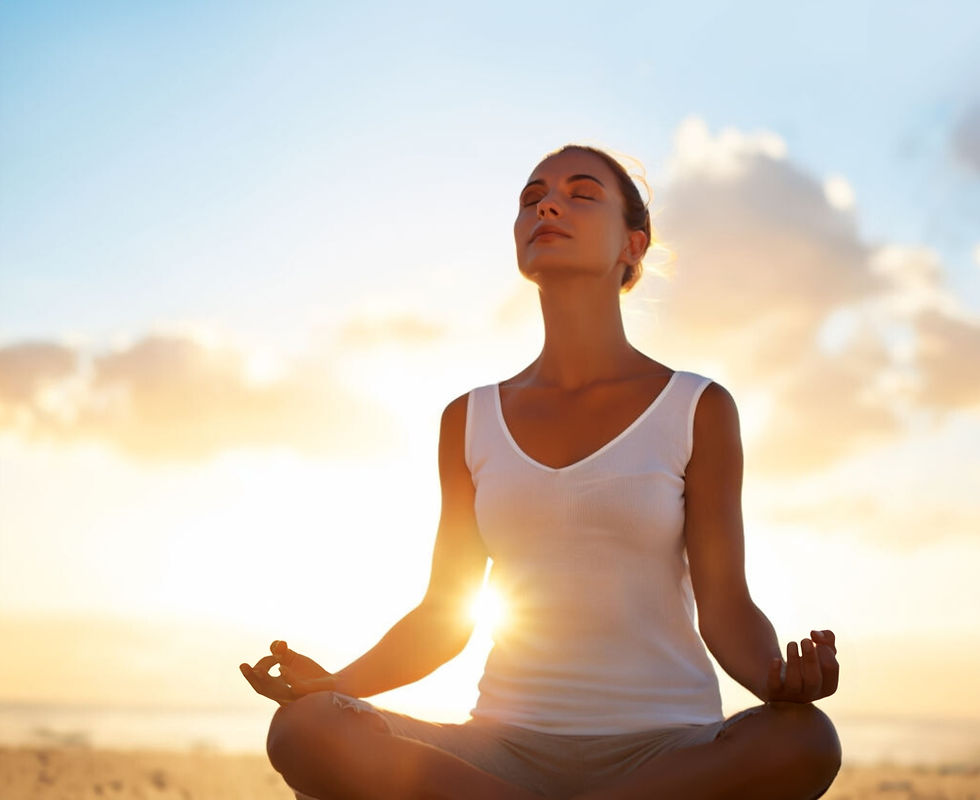 Woman meditating at sunset on a beach with white shirt on