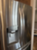 Stainless steel refrigerator with double doors and a water dispenser. Wood cabinet above, with a pet bed visible in the background.
