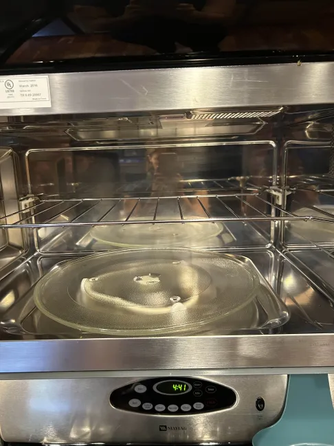 Microwave oven with open door, showing glass turntable and wire rack. Digital display shows 4:41. Stainless steel finish, reflecting surroundings.