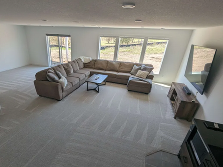 Empty modern living room with brown sectional sofa, coffee table, wall TV, large windows, and soft neutral carpet. after a deep cleaning with sparkling homes