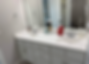 Bright bathroom with a double white vanity, large mirror, toiletries, and an open door revealing a toilet in the background.
