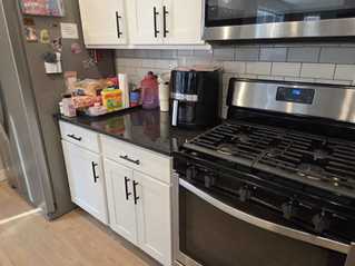 Modern kitchen with white cabinets, black stove and coffee maker, groceries on counter, and a refrigerator with magnets.