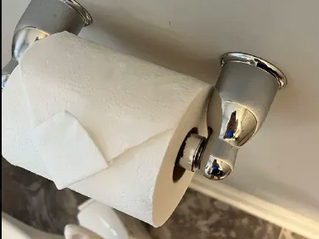 Toilet paper roll on chrome wall holder in a bathroom, with gray wall and tiled floor below. After a sparkling homes deep clean