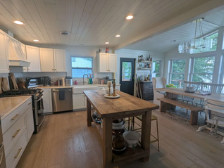 Bright modern kitchen with white cabinets, wood island, and dining nook by large windows; warm, calm, airy atmosphere.