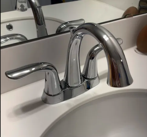 Chrome bathroom faucet over a white sink, reflected in a mirror, with soft lighting and a clean modern look.
