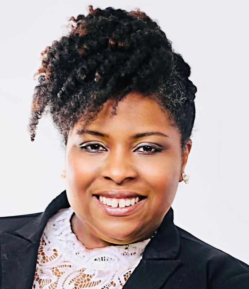 Portrait of a woman smiling, wearing a black blazer and white lace top, with natural curly hair styled up, on a light background, portrait orientation.