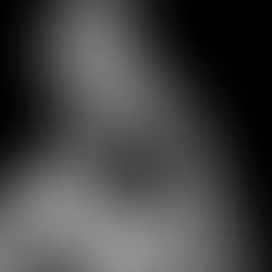Black-and-white portrait of a shirtless young man with hand on chin, gazing upward against a dark background.
