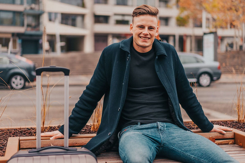 Smiling man sitting with a suitcase outdoors. 