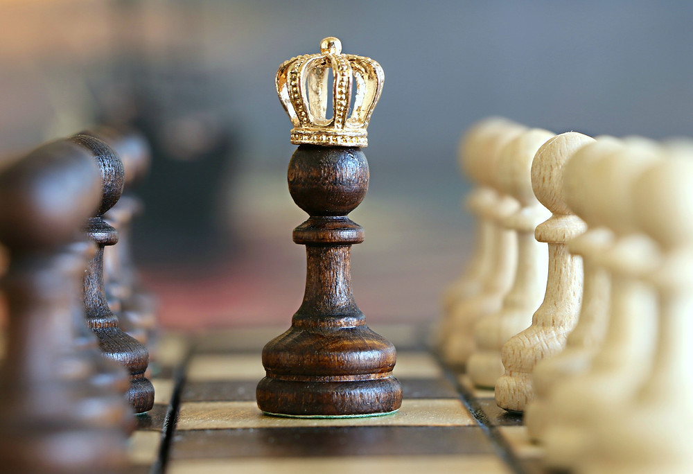 Pawn chess piece with queen's crown in the middle of the board.