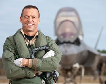Fighter Pilot, Billie Flynn, stands before a F35 in a green flight suit.