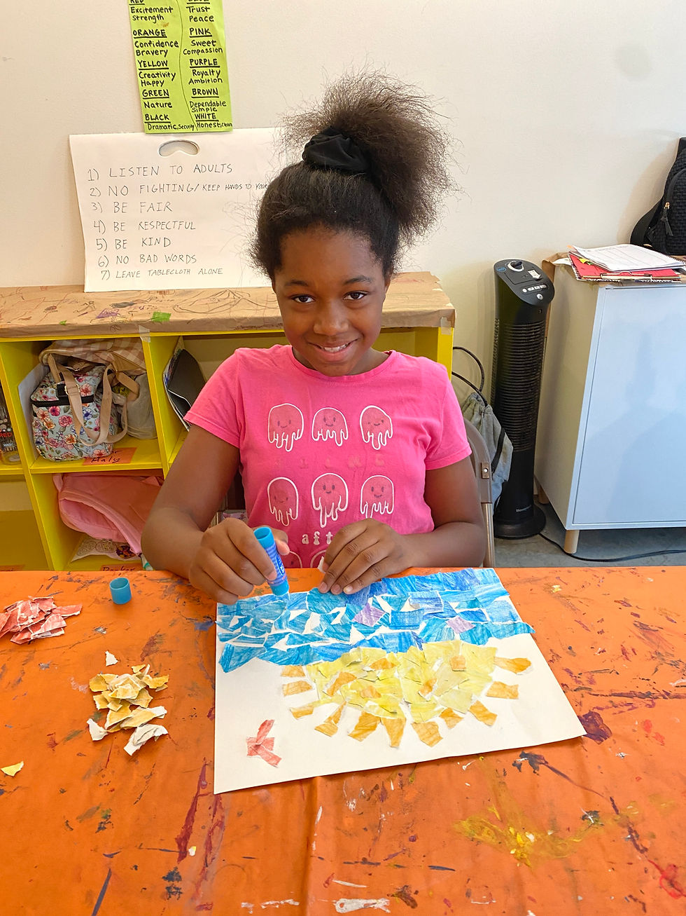 Young girl collaging a sun and water and smiling at the camera.