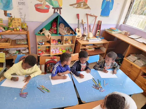 a group of four children in a classroom coloring on paper on blue desks