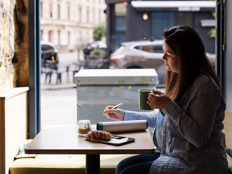 Amanda Hughes founder of the small business community by Amanda Hughes sat working by a window in a cafe holding a hot chocolate