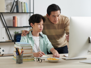 Middle aged father helping teenage son with doing homework, he is pointing at the computer screen