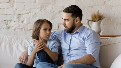 Father and child sitting on a couch having a serious conversation, showing emotional connection and support.