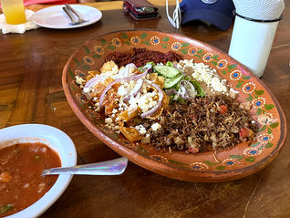 red plate of meat and sides with a white bowl of salsa