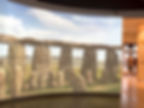 Museum exhibit shows Stonehenge-like stones on a curved screen with text 2300BC Bluestones Rearranged; a man walks by.
