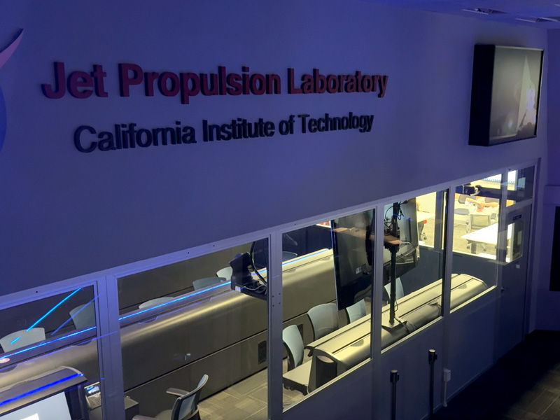 Jet Propulsion Laboratory, California Institute of Technology sign above glass-walled lab with office chairs and blue lighting