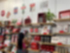 Woman in pink tank top browsing Coca-Cola merchandise in a store. Shelves display signs, bottles, and plants against a white wall.