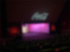 Dimly lit theater with empty seats, pink-lit walls, and a "Coca-Cola" projection on the screen, creating a calm and inviting mood.