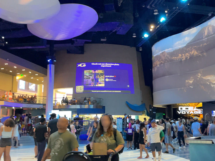 People in a bustling indoor area with digital screens and futuristic lighting. A large sign reads "Check out our showcase". Energetic mood.