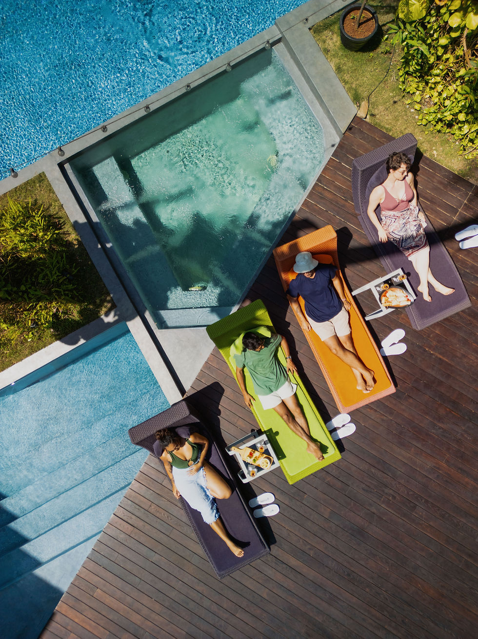 People relaxing by the pool on colorful lounge chairs in the sun.