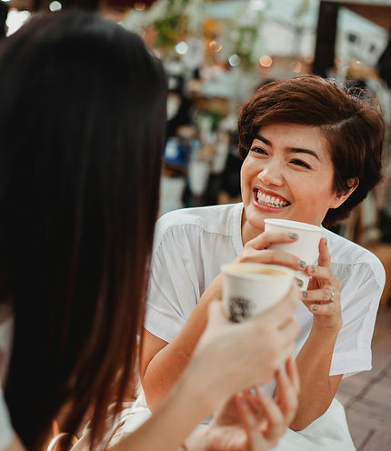 Smiling woman with short hair enjoying coffee and conversation with a friend at an outdoor café, representing connection.