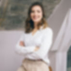 Retrato profissional de Graziella, fundadora do Estúdio K, sorrindo com confiança e os braços cruzados. Ela veste uma camisa 