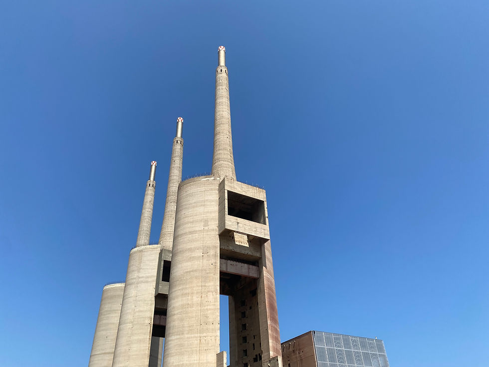 Landscape photo of three tall concrete industrial chimneys and a rectangular tower against a clear blue sky, wide landscape orientation, minimalistic composition, Barcelona industrial landmark.