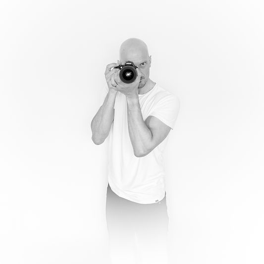 Black and white self portrait of Dan, the photographer aiming his camera at the lens.