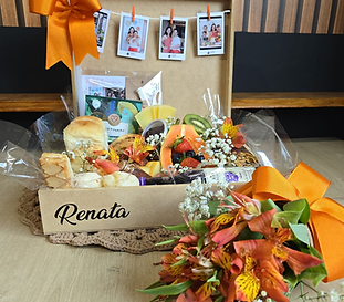 Maleta personalizada aberta com seleção gourmet, laços laranja, frutas, queijos e fotos Polaroid.