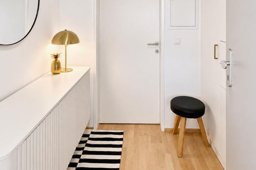 Heller Eingangsbereich mit weißem Sideboard, deckenhohem Einbauschrank, goldener Tischleuchte und ausgewählten Wohnaccessoires.