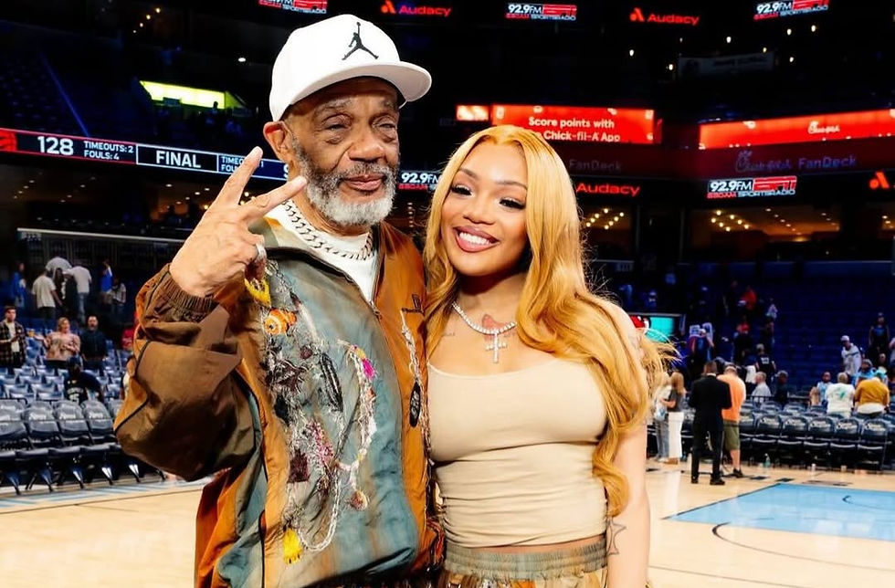 Man and woman in matching artistic outfits pose on a basketball court. The man flashes a peace sign; the woman smiles brightly.